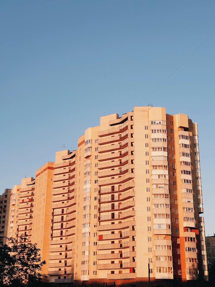 Stunning low angle view of a modern apartment building with glass panels set against a clear blue sky at sunset.