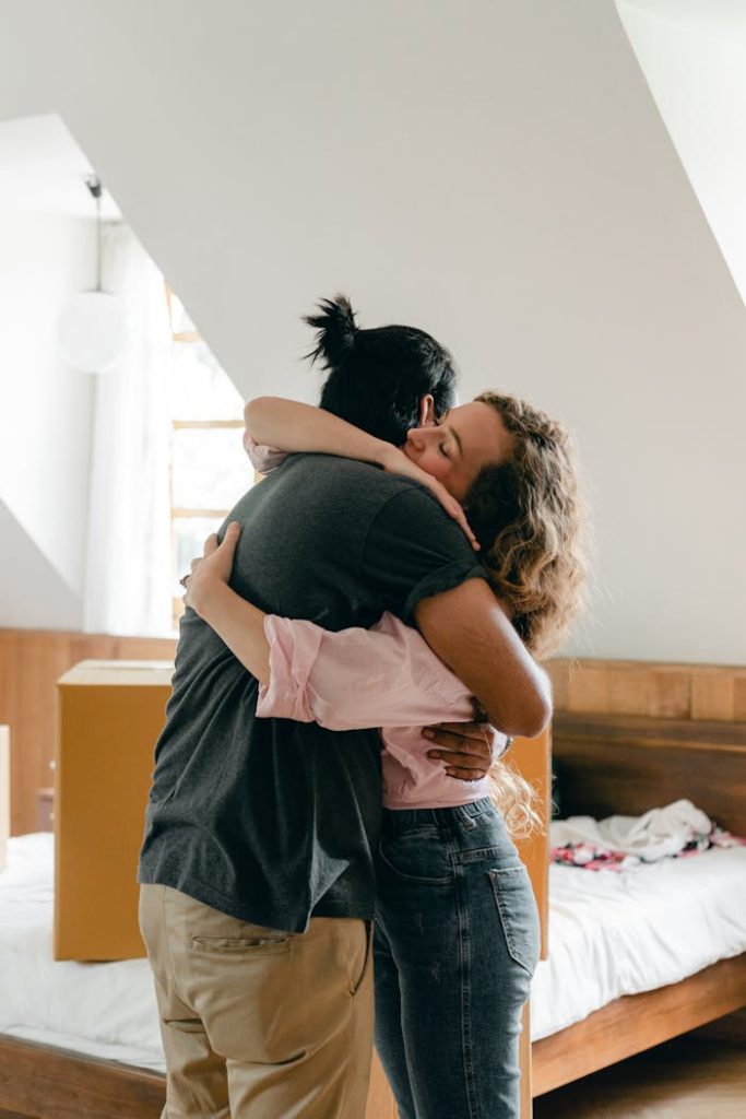 pexels photo 4246058 1 Loving young couple embracing while standing in cozy attic bedroom near bed with unpacked cardboard box while moving in new house
